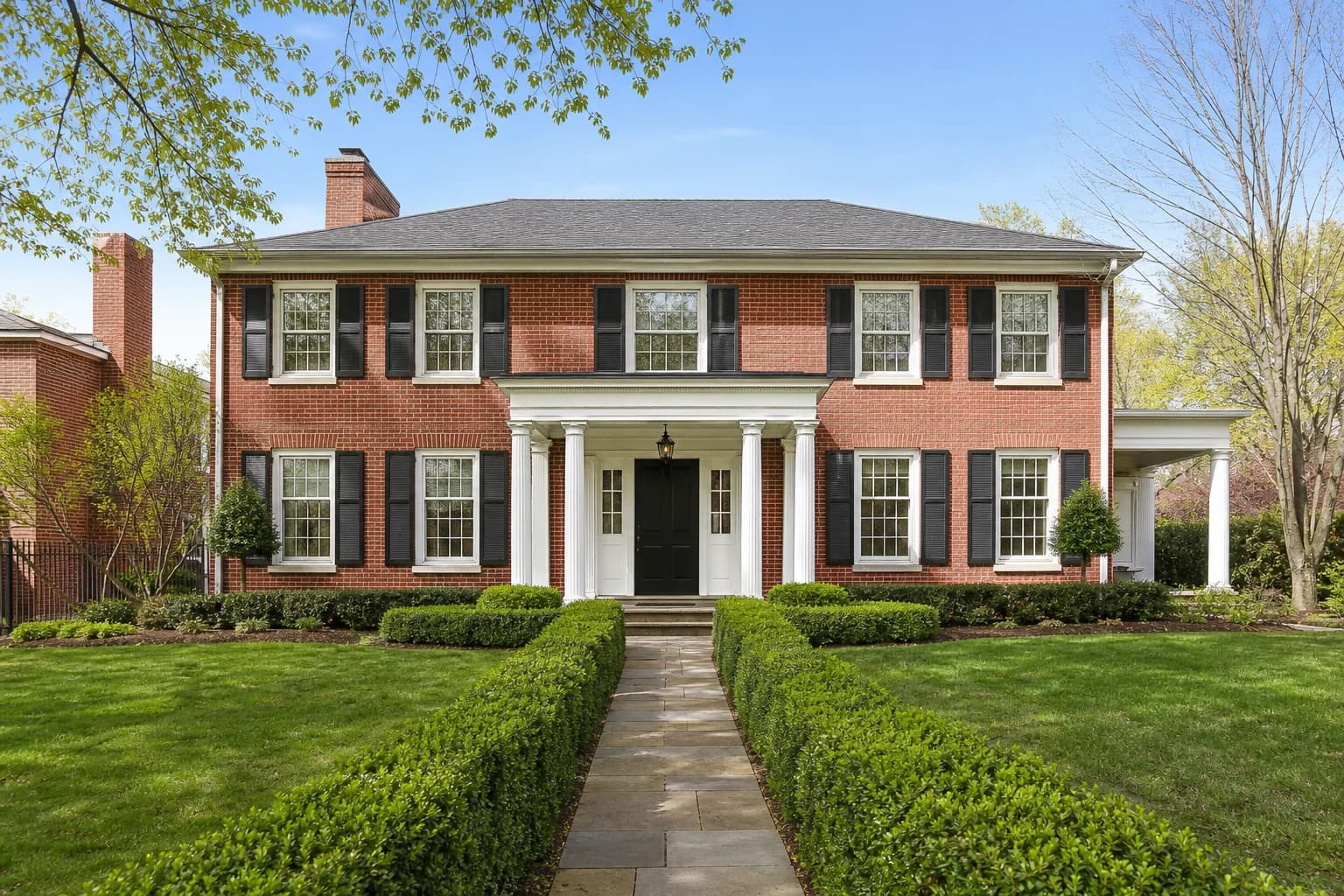 Classic colonial revival brick home with manicured boxwood hedges
